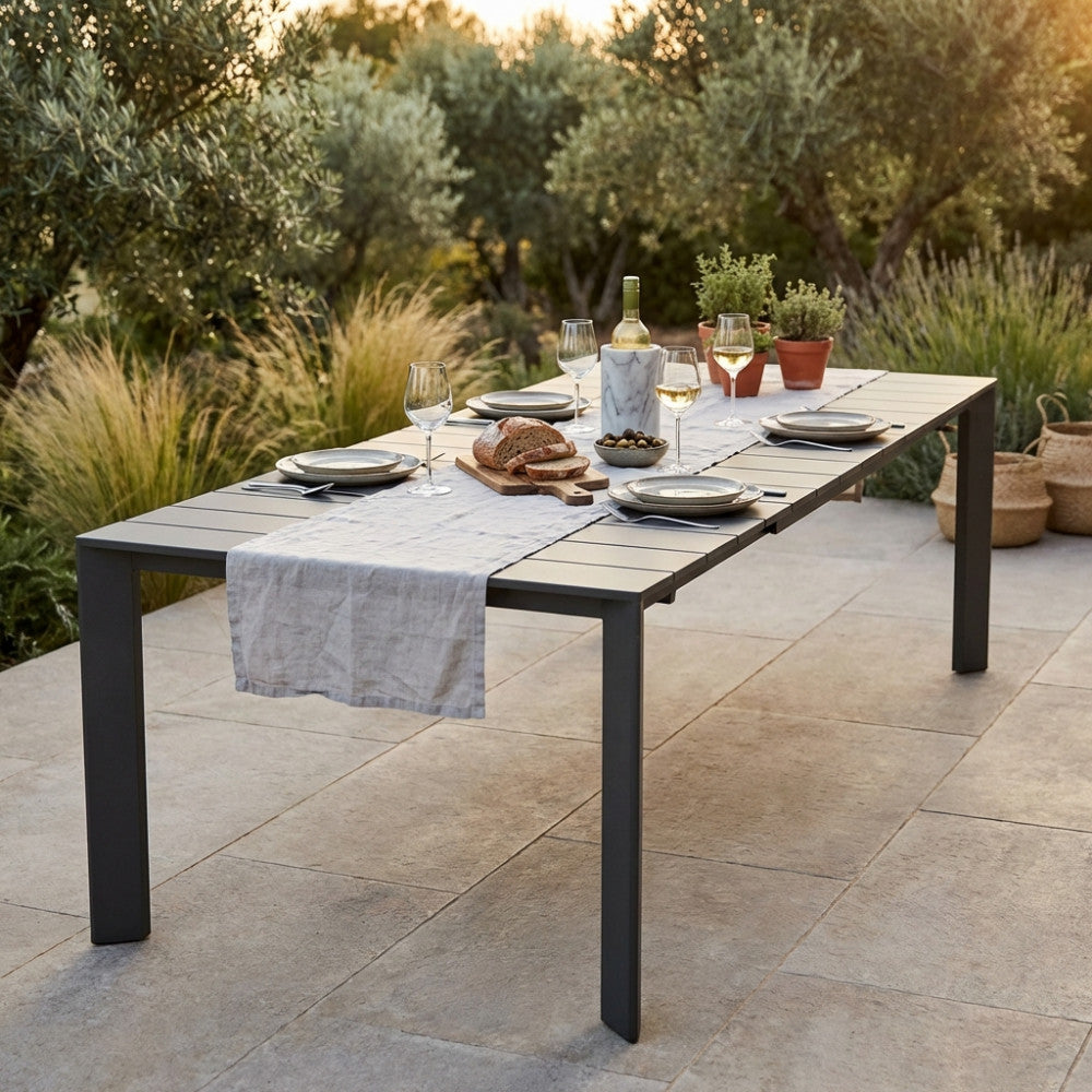 Tavolo da giardino allungabile Sacramento in alluminio taupe allestito per un pranzo all'aperto con runner in lino e calici di vino.