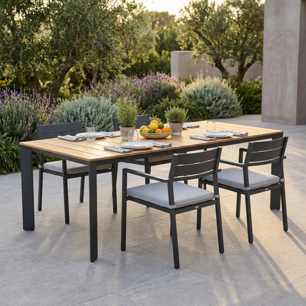Dettaglio del tavolo in teak Tulcán con sedie coordinate in un rigoglioso giardino moderno.