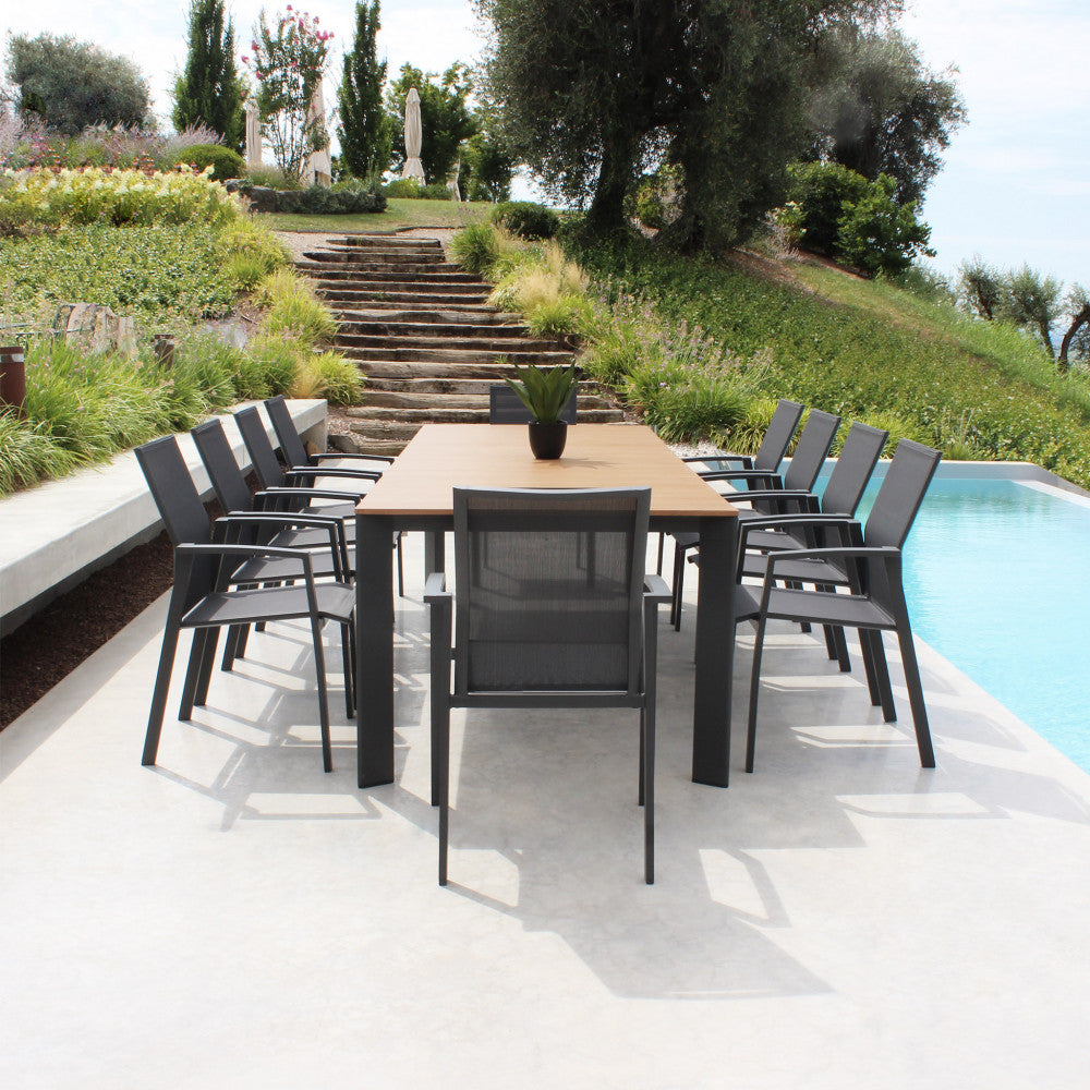 Vista frontale del tavolo in teak Tulcán allungato con dieci sedute a bordo piscina.
