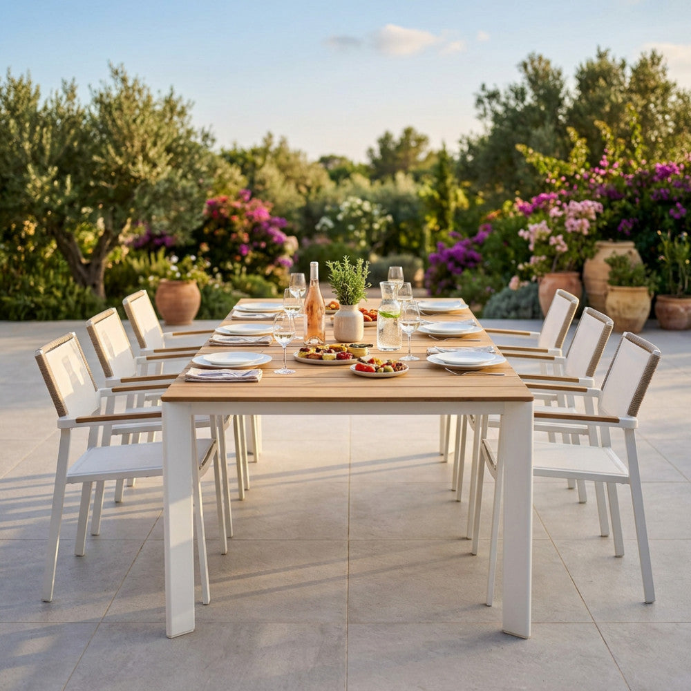 Grande tavolo da pranzo in teak Tulcán circondato da dieci sedie bianche in un rigoglioso giardino.