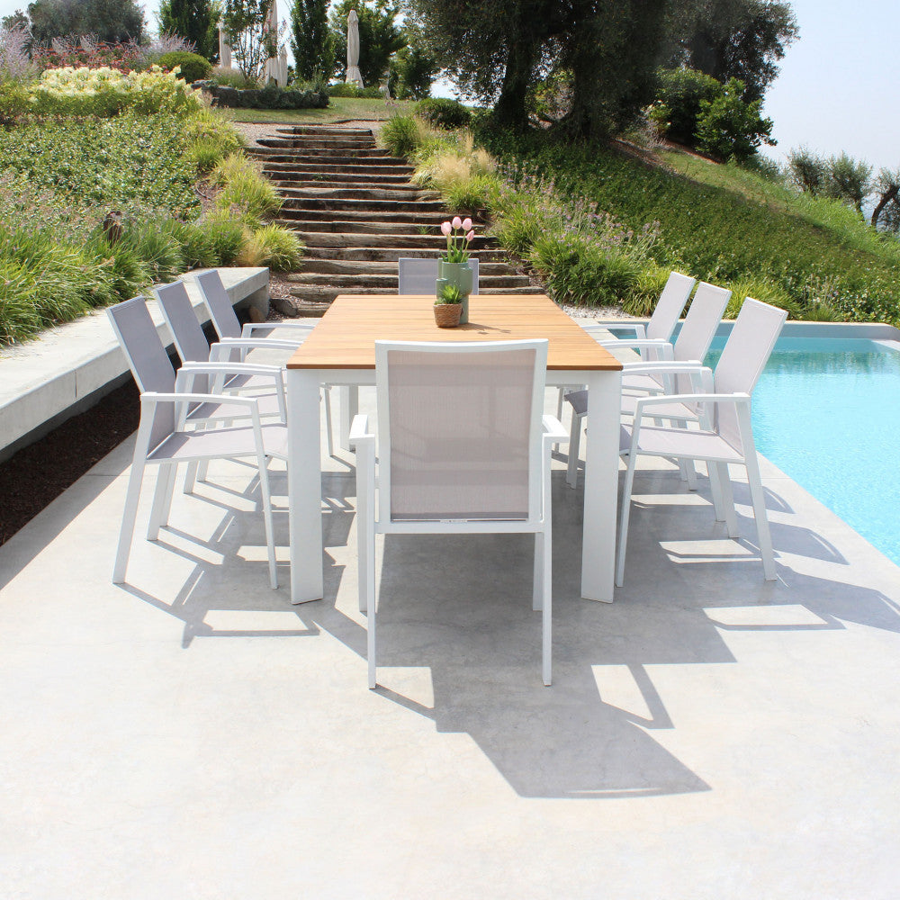 Tavolo da pranzo Tulcán in teak allestito a bordo piscina con gradini in pietra sullo sfondo.