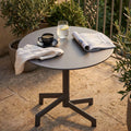 Tavolo da giardino rotondo in acciaio taupe allestito con caffè e rivista su un patio in pietra.