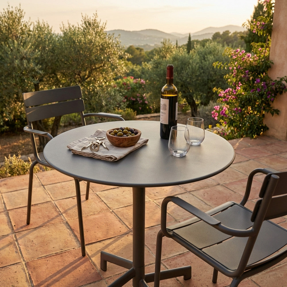 Tavolo da esterno in acciaio taupe con sedie abbinate, vino e olive su una terrazza panoramica.