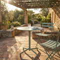Tavolo da giardino in acciaio verde menta allestito su un patio in cotto illuminato dal sole.