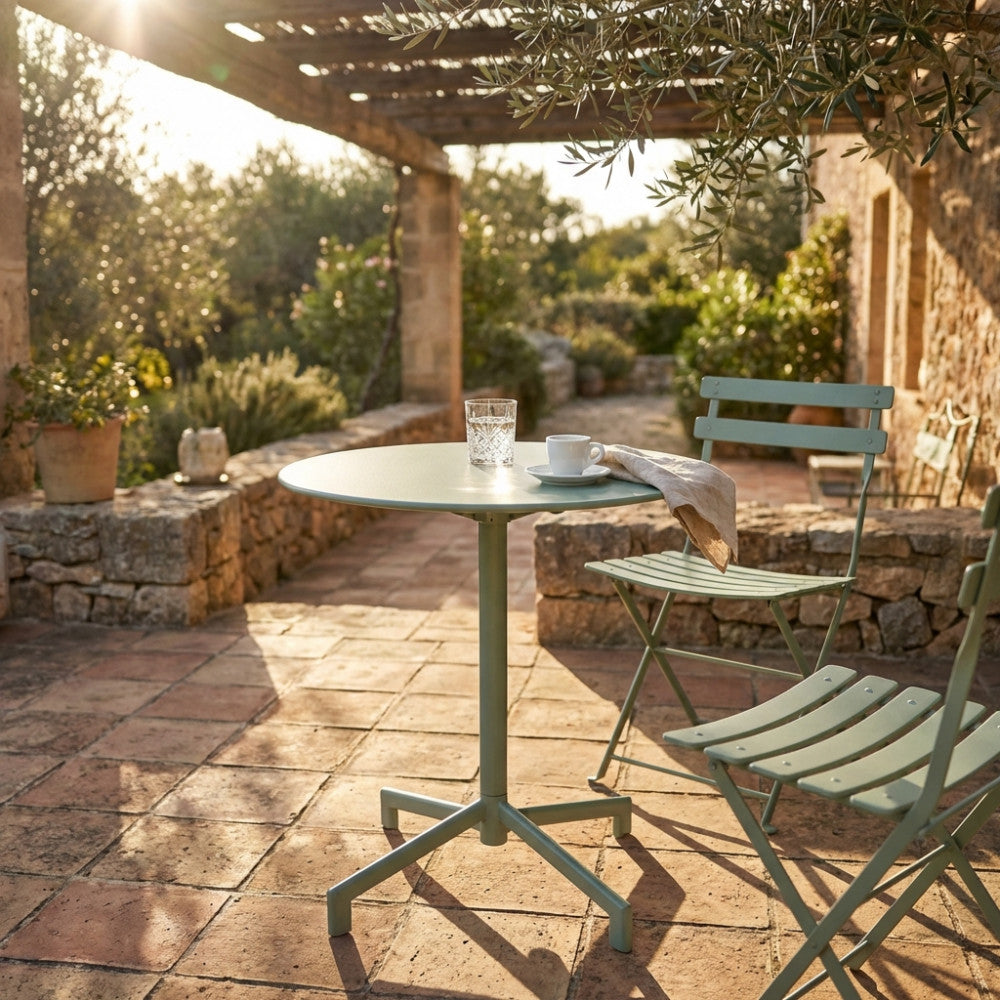 Tavolo da giardino in acciaio verde menta allestito su un patio in cotto illuminato dal sole.
