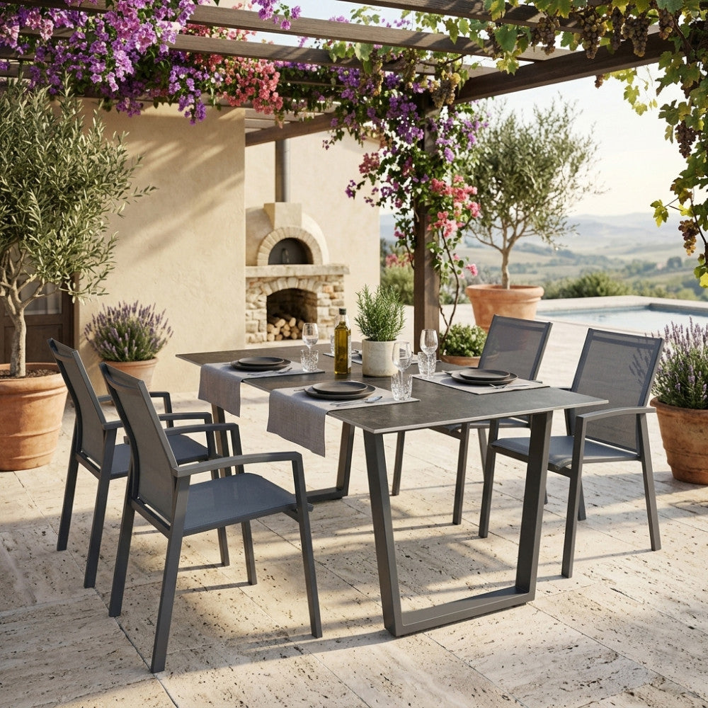Tavolo da giardino Warren 2 in alluminio e pietra sinterizzata antracite, allestito sotto un pergolato fiorito con sedute abbinate.