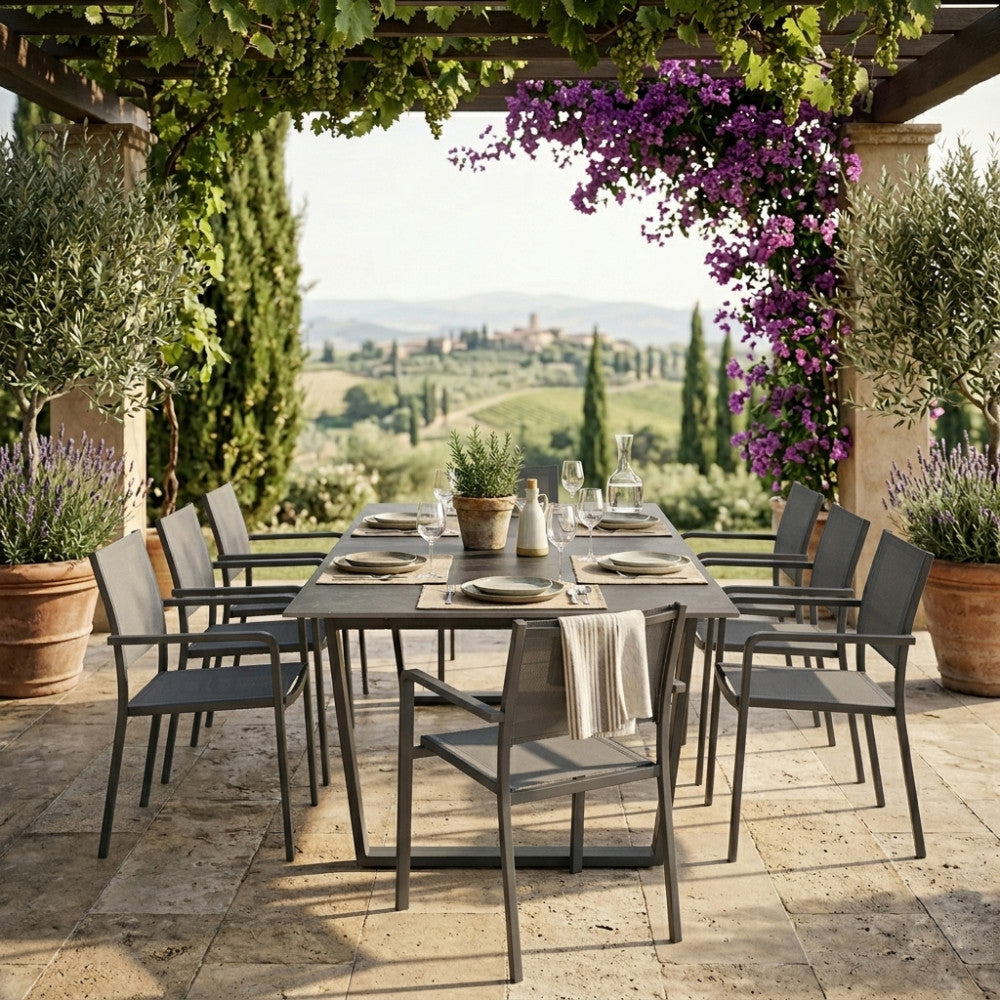 Tavolo da esterno Warren 2 con piano in pietra scura, circondato da sedie moderne in un elegante patio con vista panoramica.