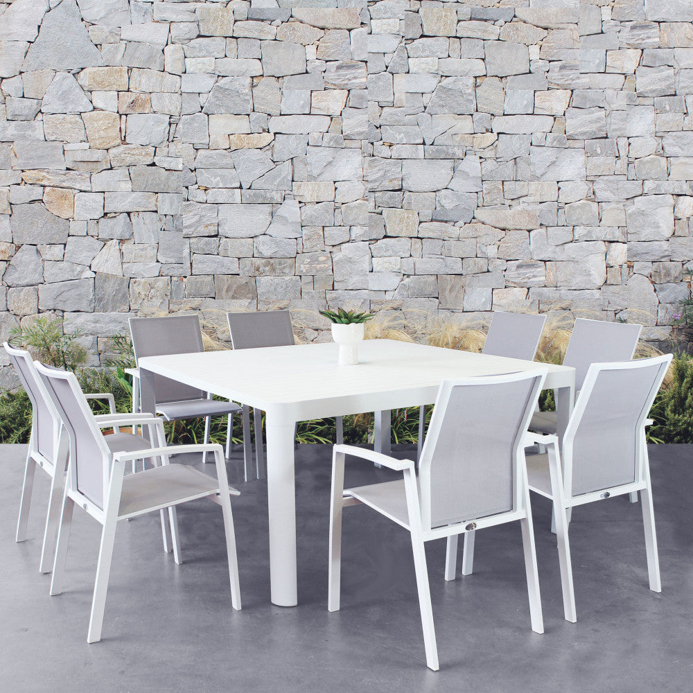 Tavolo da giardino Washington allungabile in alluminio bianco, circondato da sedie moderne, posizionato davanti a un muro in pietra.