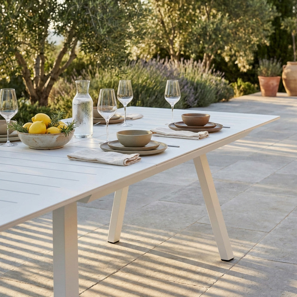Dettaglio della superficie a doghe del tavolo Zante bianco con mise en place elegante e limoni freschi.