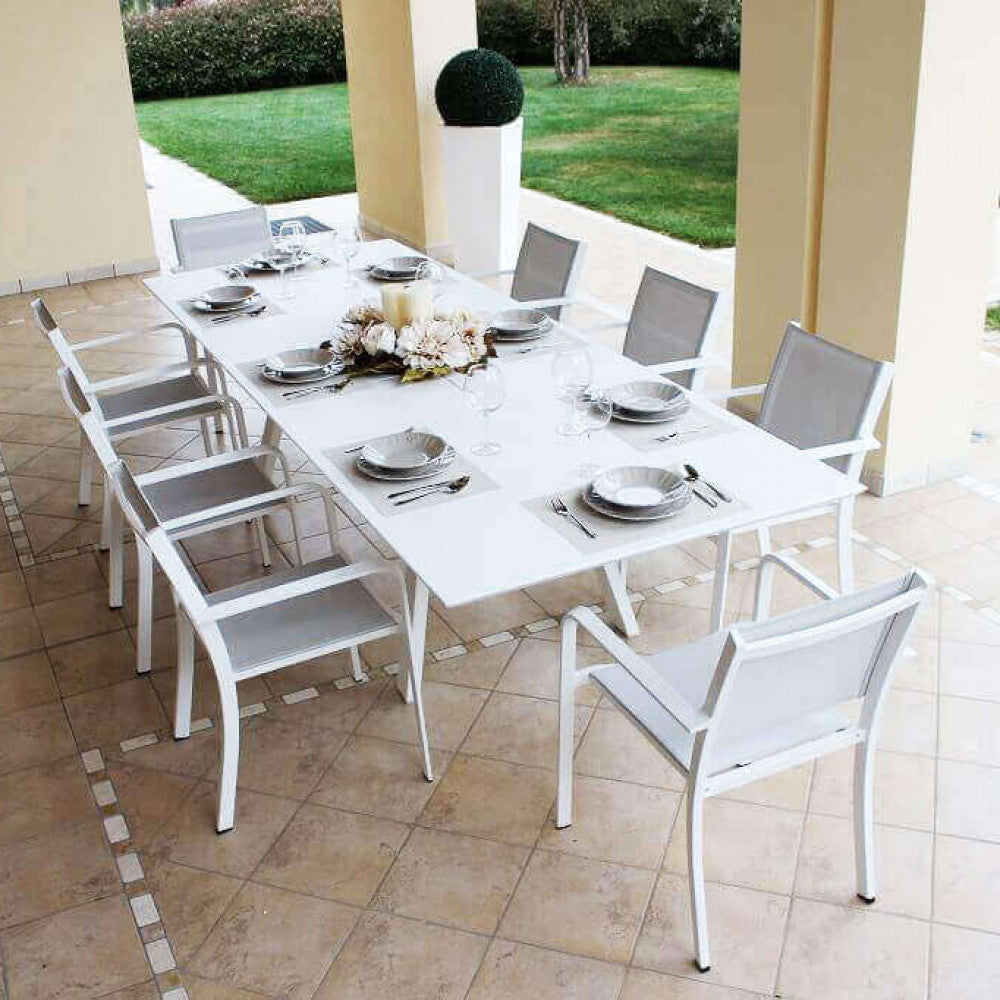 Tavolo Zante allestito sotto un porticato con otto sedie abbinate e decorazione floreale centrale.