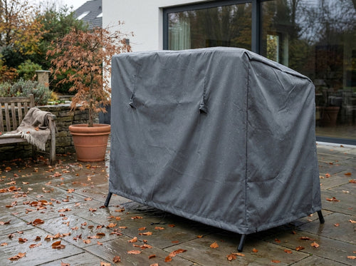 Telo di copertura per dondolo in tessuto antracite posizionato su un patio in pietra bagnato dalla pioggia.