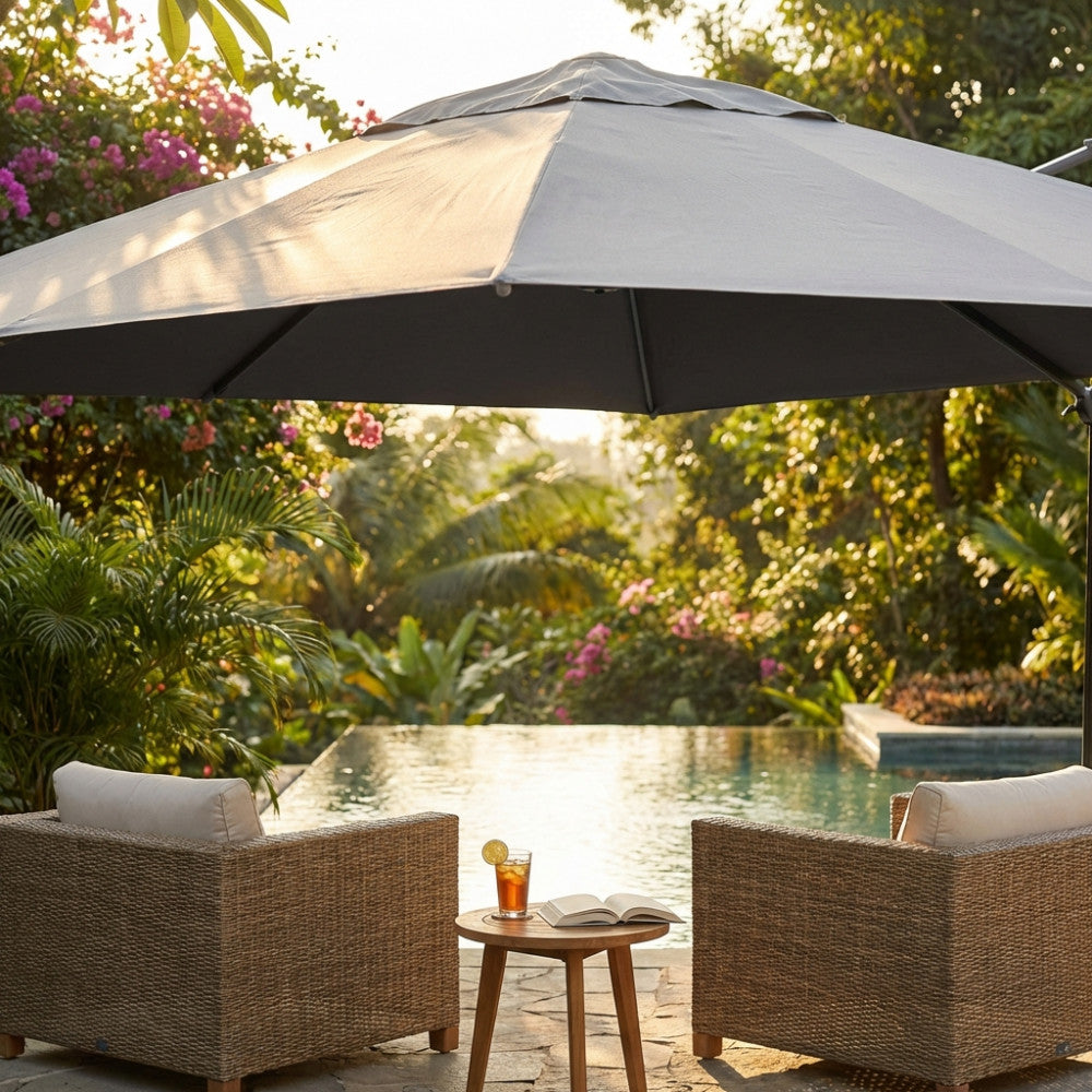 Copertura per ombrellone grigia 5x5 metri sopra due poltrone in rattan a bordo piscina in un giardino tropicale.
