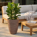 Vaso Grande Anemone color taupe in fibra sintetica, allestito in un patio esterno con pianta verde, divano in legno e tavolino.