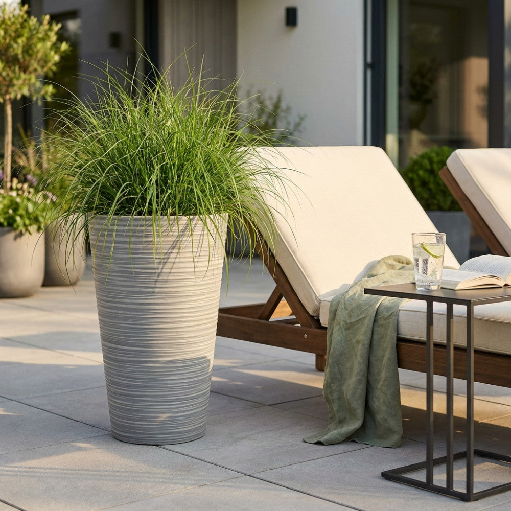 Vaso Grande Azalea in fibra sintetica antracite posizionato su un patio moderno accanto a un lettino prendisole.