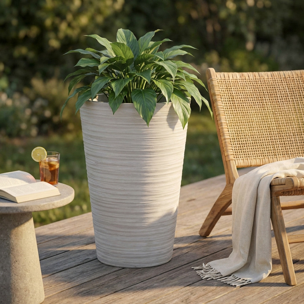 Vaso grande in fibra sintetica bianca con pianta verde su un patio in legno, accanto a una sedia in rattan.