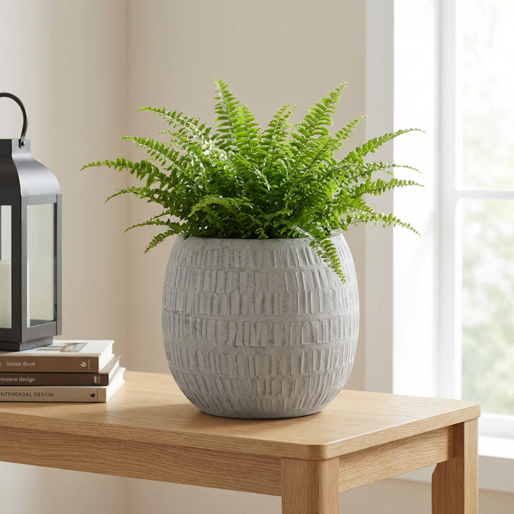 Vaso scultoreo grigio con felce rigogliosa, elegantemente esposto su un tavolo in legno chiaro.