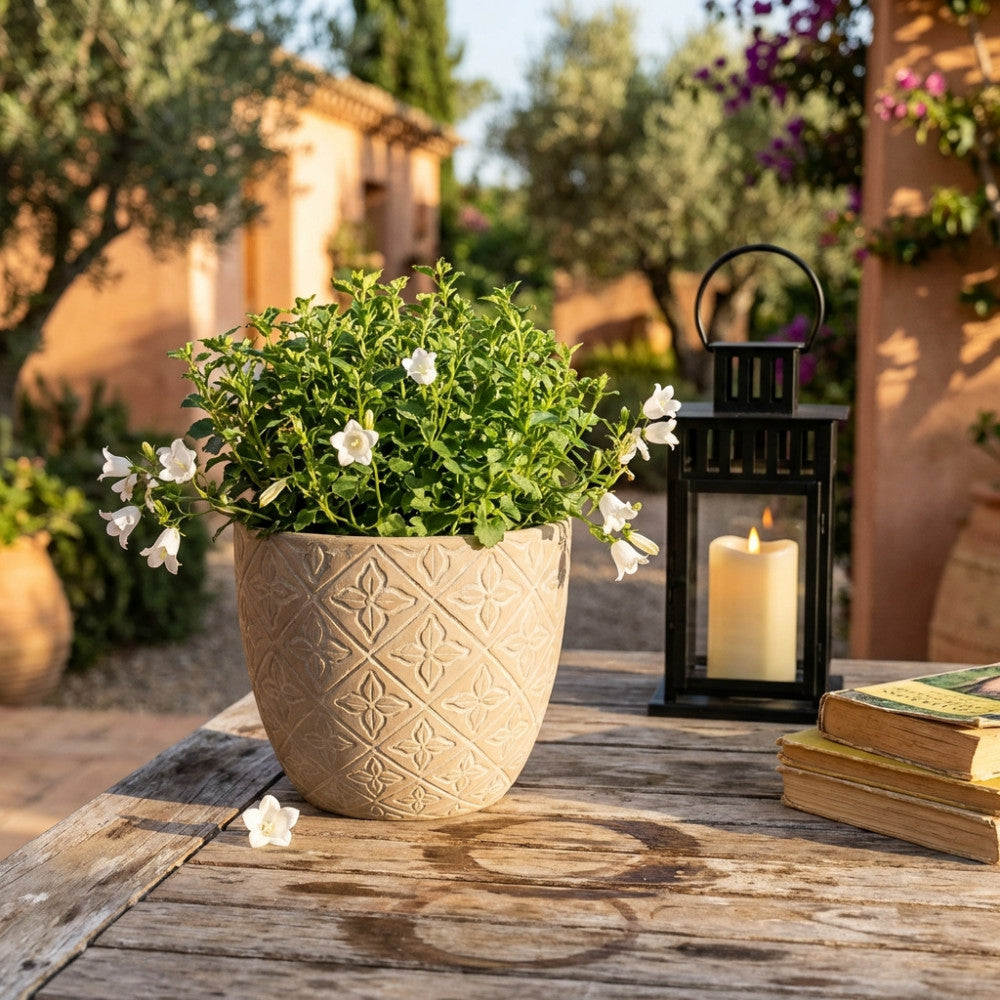 Vaso decorativo Pansè marrone ospita fiori bianchi, allestito su un tavolo rustico in legno con una lanterna nera in un giardino mediterraneo.