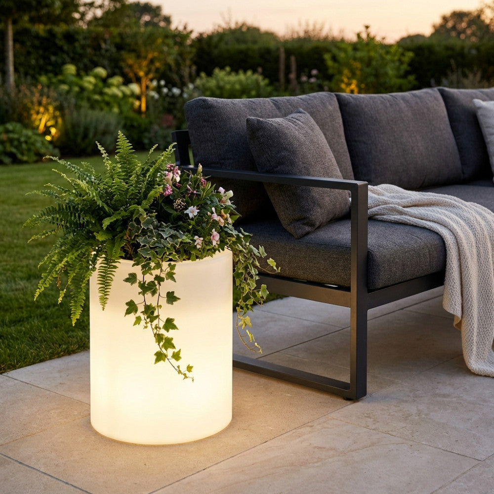 Vaso luminoso da esterno accanto a un divano grigio scuro, contenente felci e piante ricadenti.