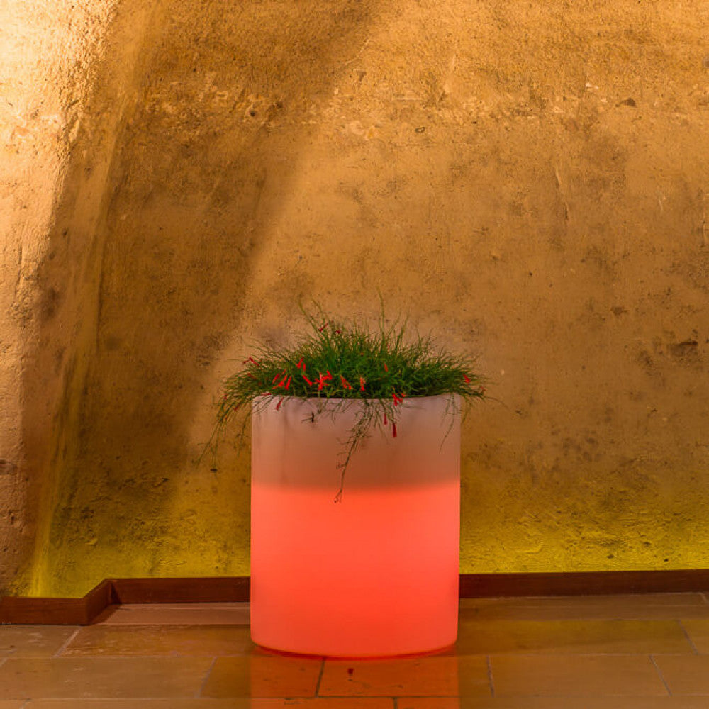 Vaso luminoso cilindrico acceso con luce rossa vibrante, che illumina una parete in tufo.