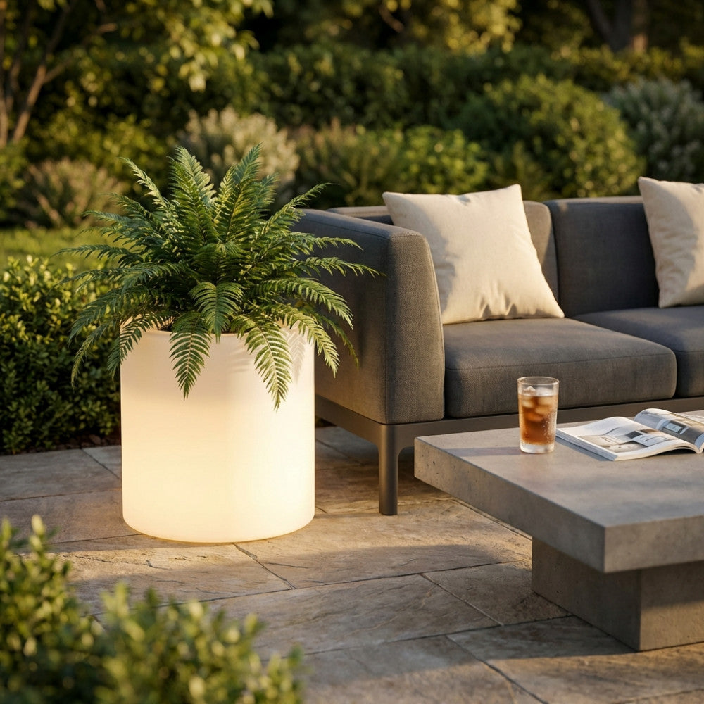 Vaso luminoso da 50 cm con felce verde accanto a un divano outdoor di lusso e tavolino in cemento.