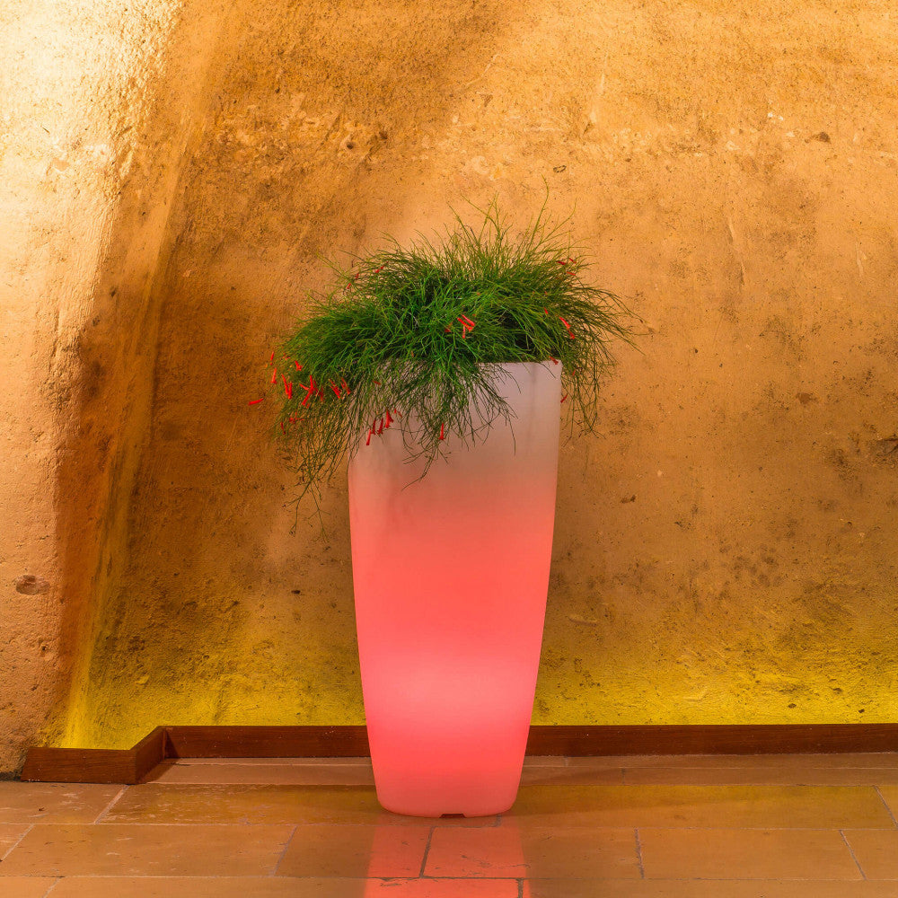 Fioriera luminosa in polipropilene con LED rosso vibrante, che crea un contrasto cromatico in un ambiente in pietra.