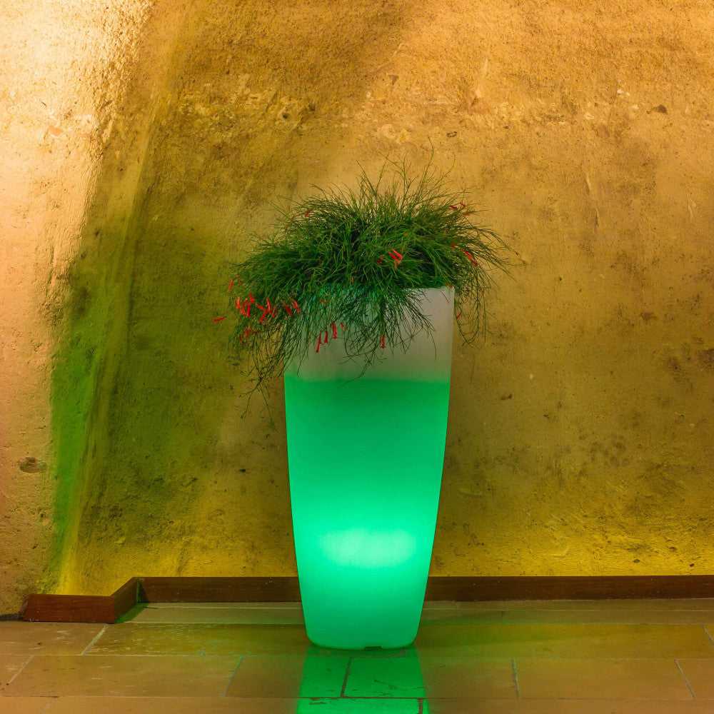 Vaso luminoso di 70 cm con LED verde smeraldo, che illumina un angolo architettonico dalle texture grezze.