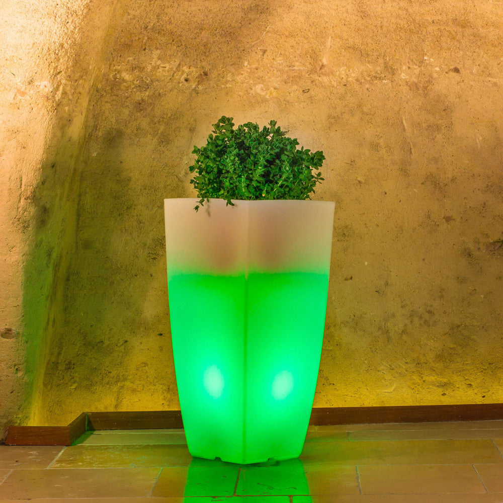 Vaso luminoso Hydrus illuminato di verde smeraldo, che esalta il contrasto cromatico con l'architettura rustica circostante.