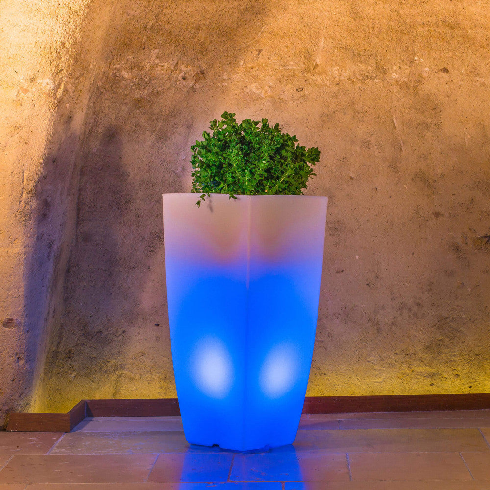 Vaso luminoso scenografico con luce blu cobalto, posizionato su un pavimento in cotto all'interno di una suggestiva cornice in pietra.