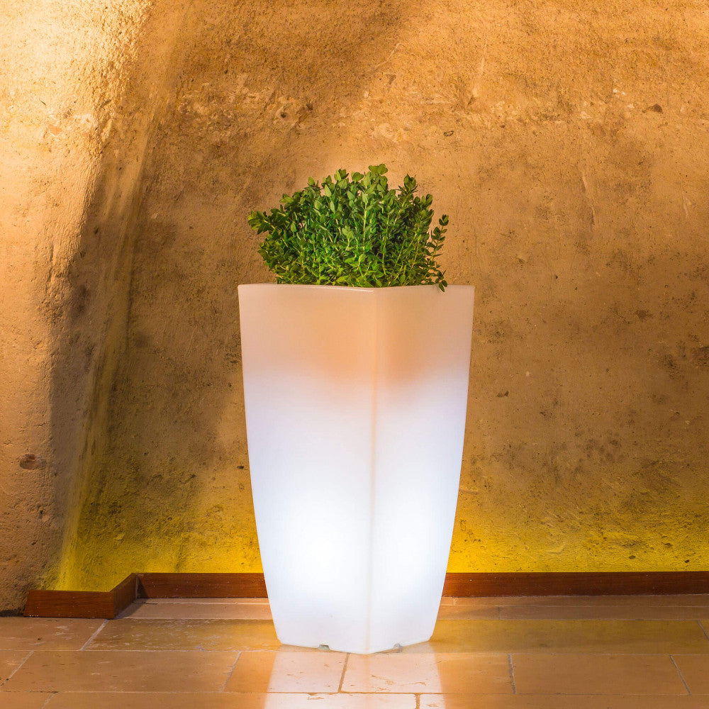 Vaso luminoso in polipropilene collocato in un ambiente rustico con pareti in pietra, creando un caldo contrasto visivo.