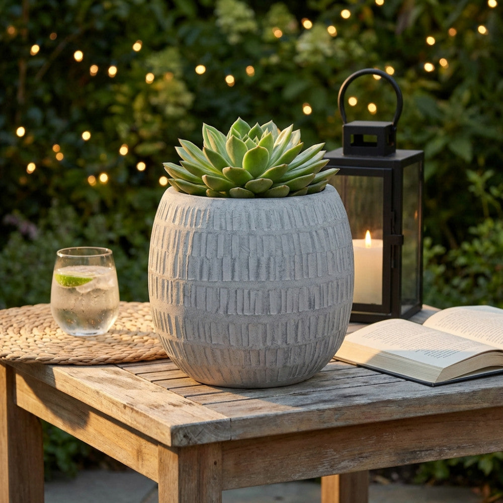 Vaso medio Betulla in fibra sintetica grigia, posizionato su un tavolo in legno all'aperto con una pianta grassa, illuminato da luci calde.