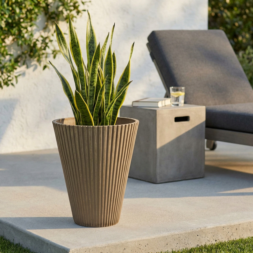 Vaso Medio Iris color taupe in fibra sintetica con pianta verde, posizionato su una terrazza in cemento accanto a un lettino prendisole.