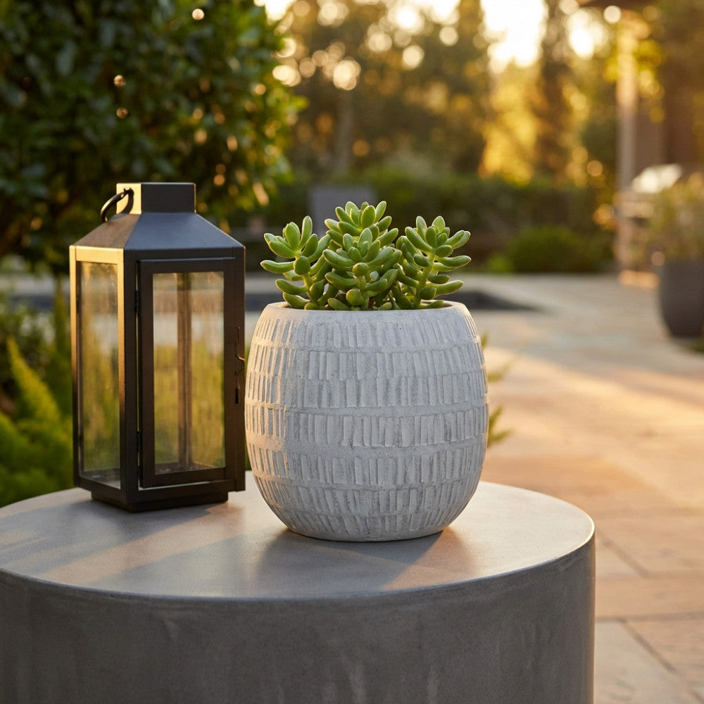 Vaso decorativo grigio con texture incisa posizionato su un tavolino in cemento durante la golden hour.