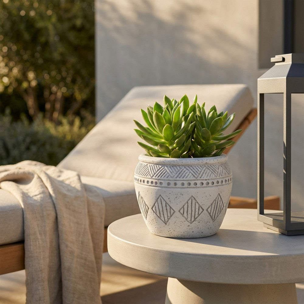 Vaso piccolo in fibra sintetica grigia con pianta succulenta, posizionato su un tavolino da esterno in cemento sotto la luce naturale.