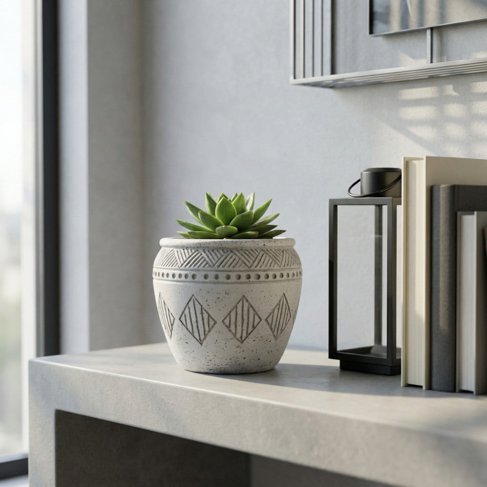 Vaso geometrico grigio decorato con rombi, collocato su una consolle interna accanto a libri e una lanterna nera.