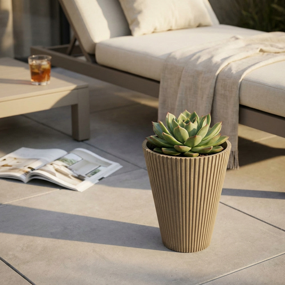 Vaso Piccolo Iris in fibra sintetica con pianta verde, appoggiato su una pavimentazione in gres porcellanato vicino a un'area lounge.