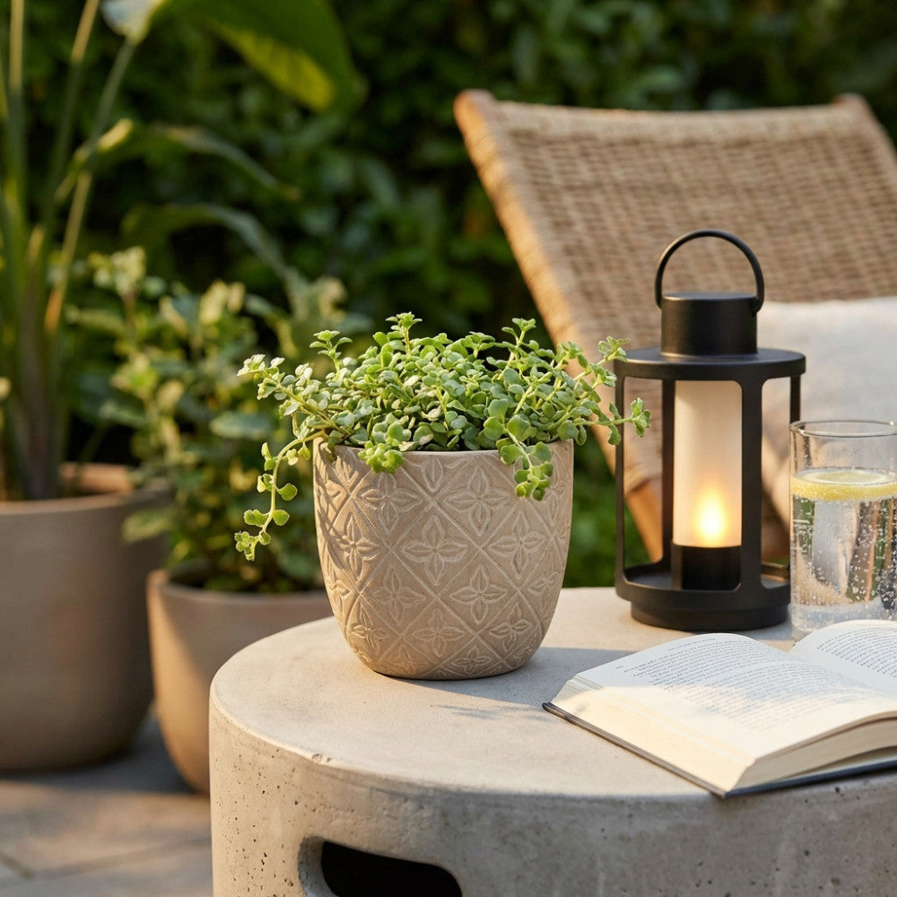 Vaso Piccolo Pansè marrone con pianta ricadente, ambientato su un tavolo da giardino con lanterna e libro.