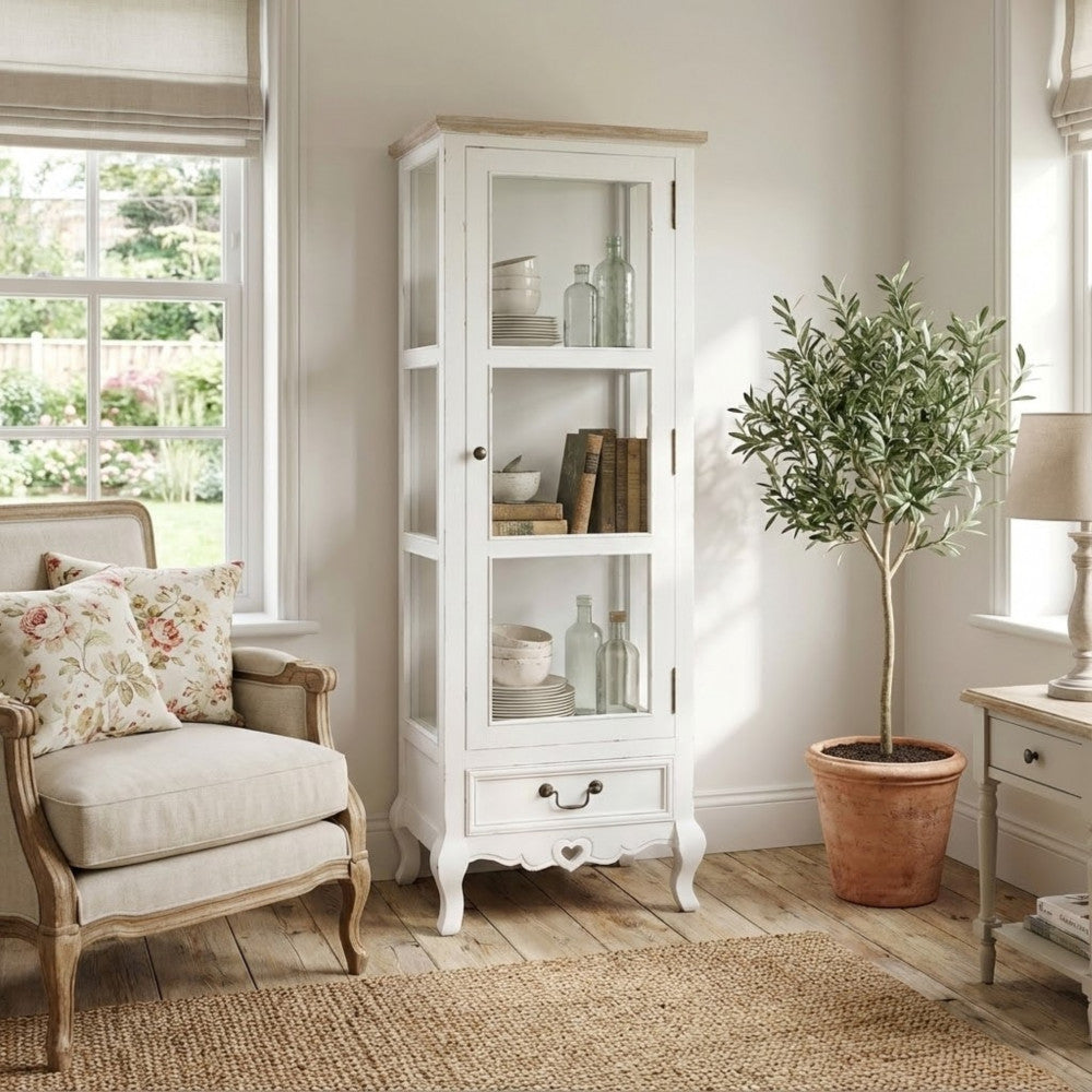 Vetrina ambientata in un luminoso soggiorno dal design rustico chic, affiancata da una poltrona e una pianta decorativa.